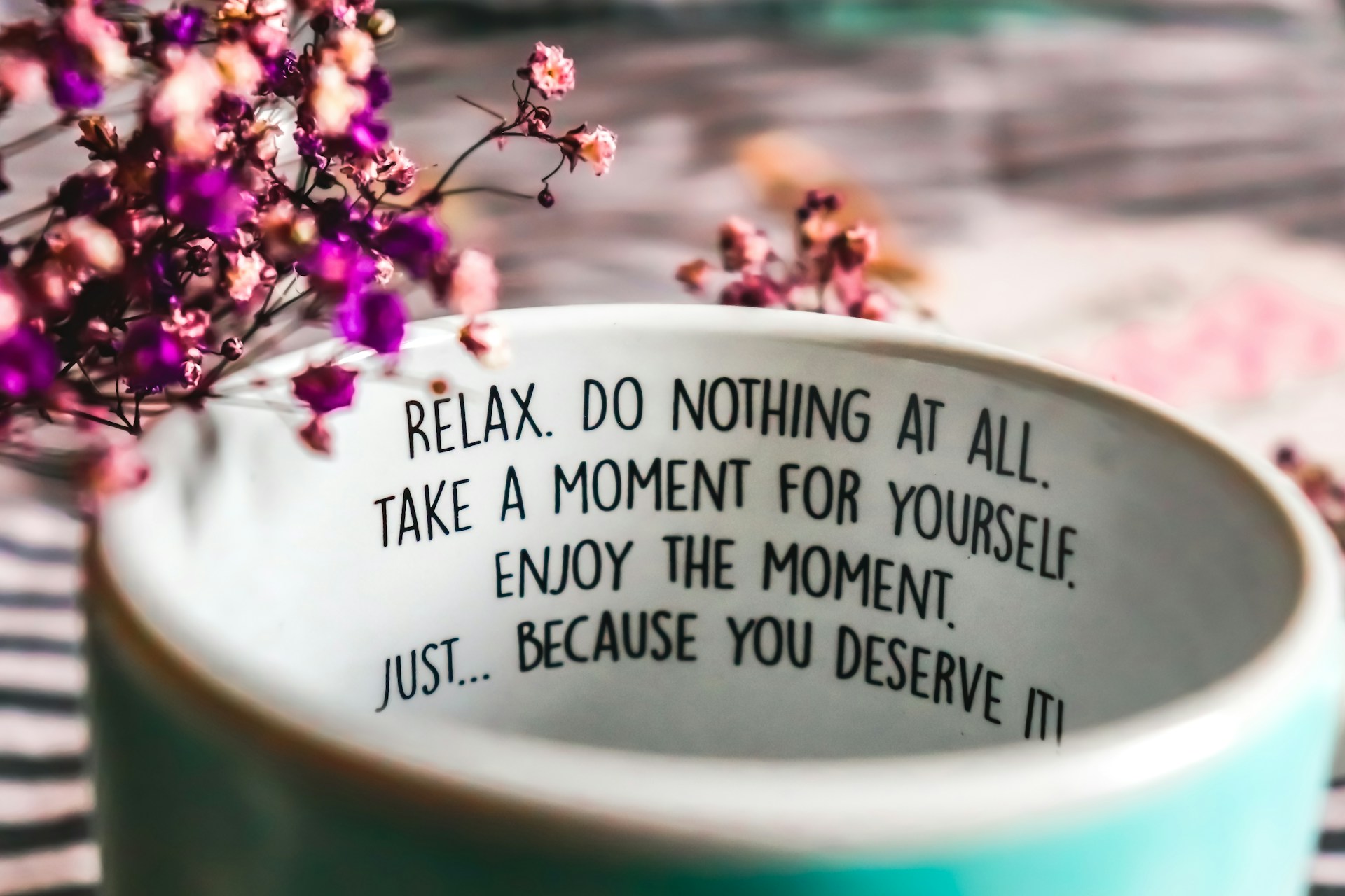 A mug with the words "Relax. Do nothing at all. Take a moment for yourself" surrounded by dried flowers.