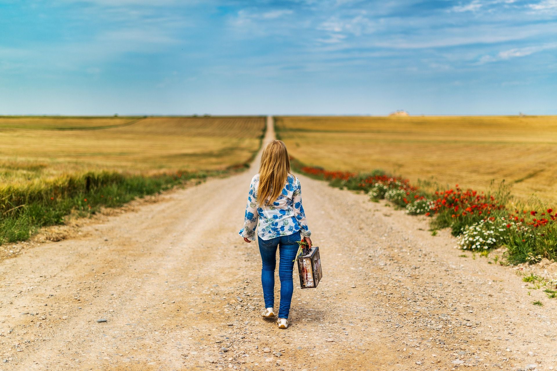Woman walking down a country road with her suitcase on her midlife magic journey