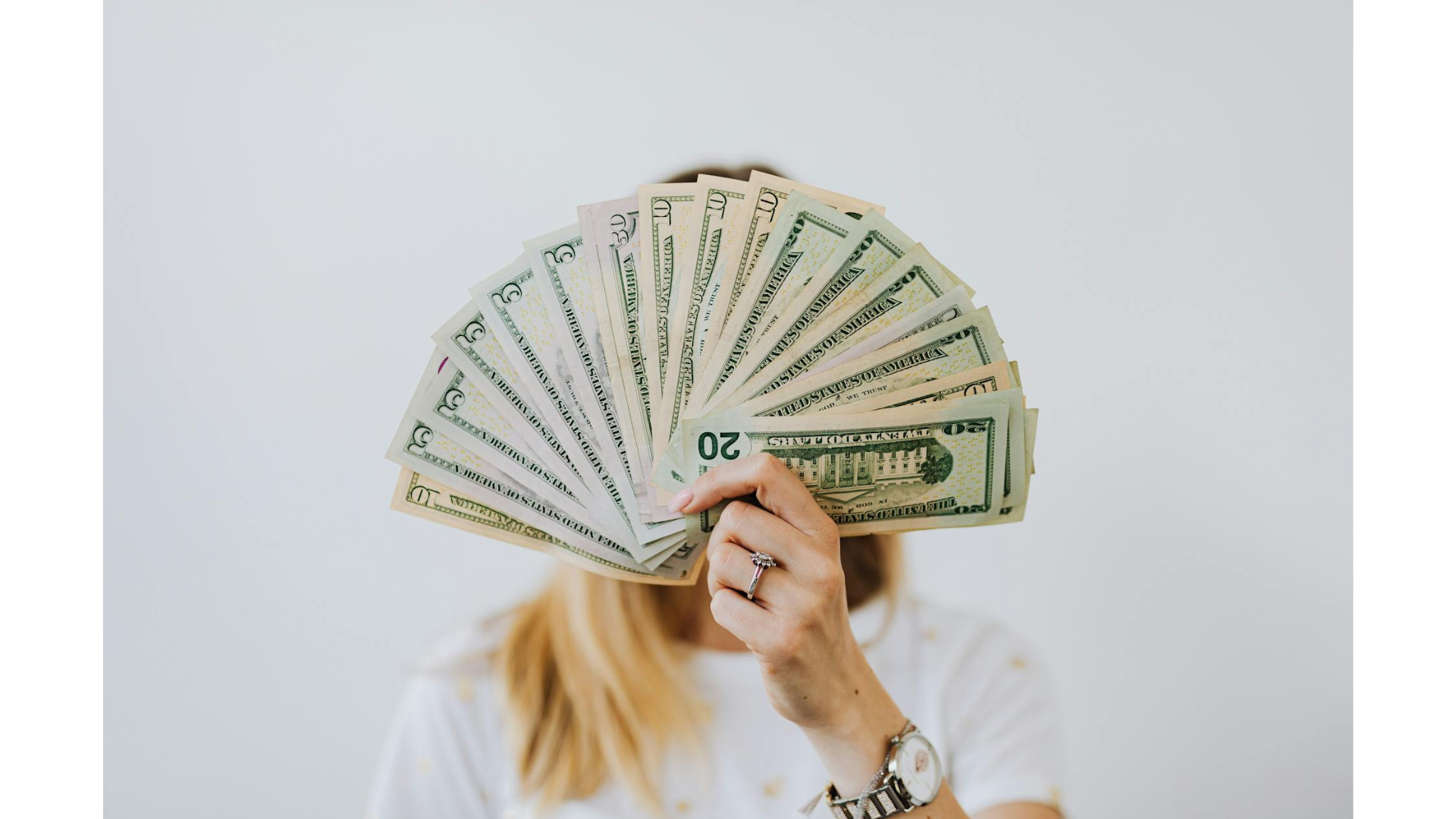 a woman holding a 'fan' of money in front of her face. Do you have limiting beliefs about money?